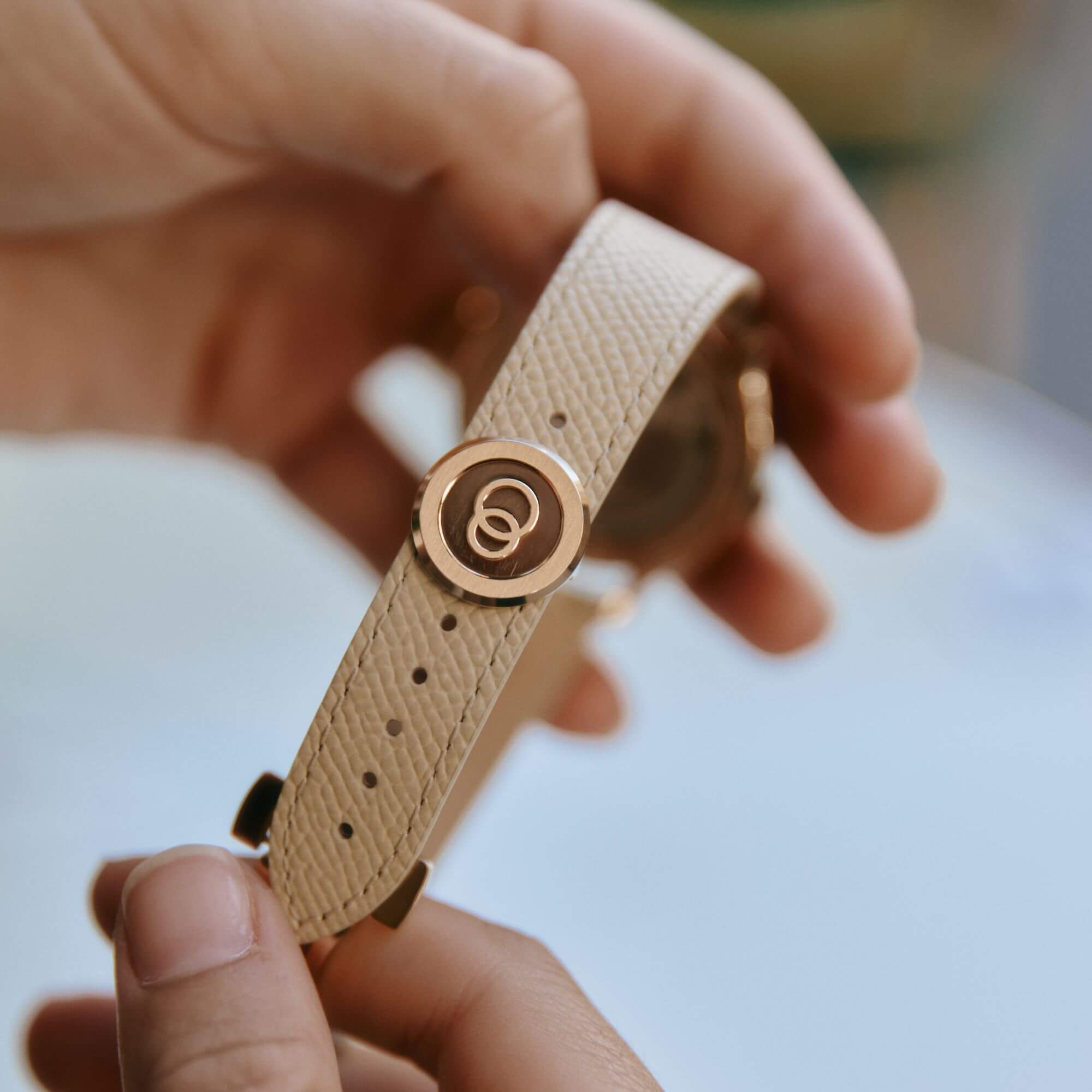 Bracelet crème grainé avec boucle or rose tenu entre deux mains