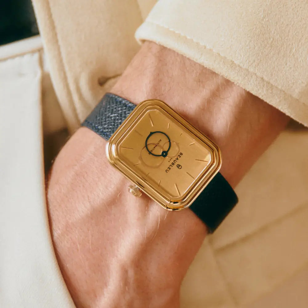 Montre carrée Figura Sienna au boîtier en or rose et cadran brossé, portée sur un poignet masculin avec un bracelet bleu grainé