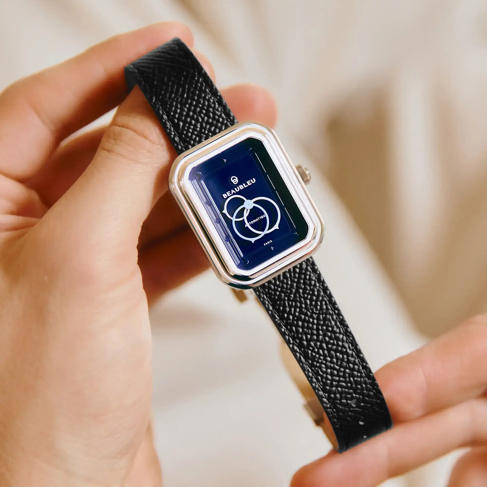 Montre Ecce Figura Smalt au cadran bleu nuit, tenue délicatement entre deux doigts, avec un bracelet en cuir noir grainé