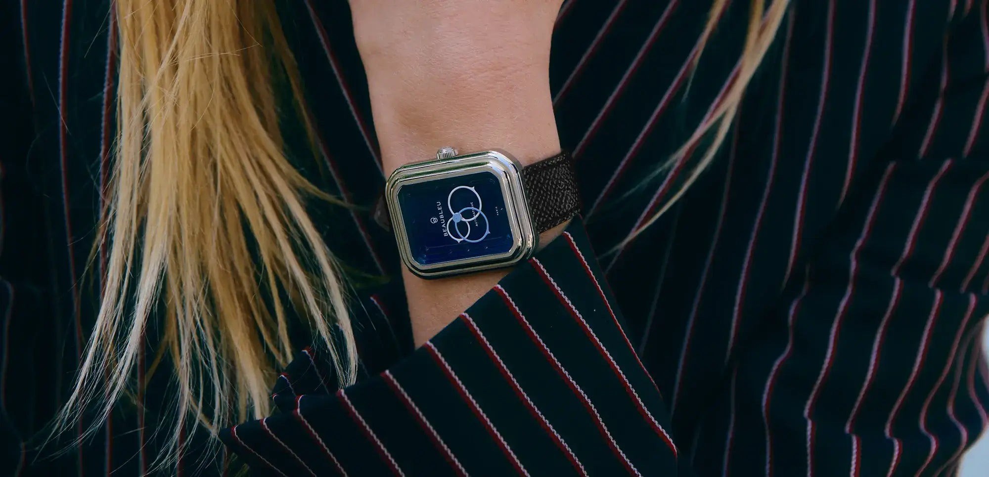 Montre Ecce Figura sur un poignet féminin, vêtue d’un haut rayé bleu marine et rouge