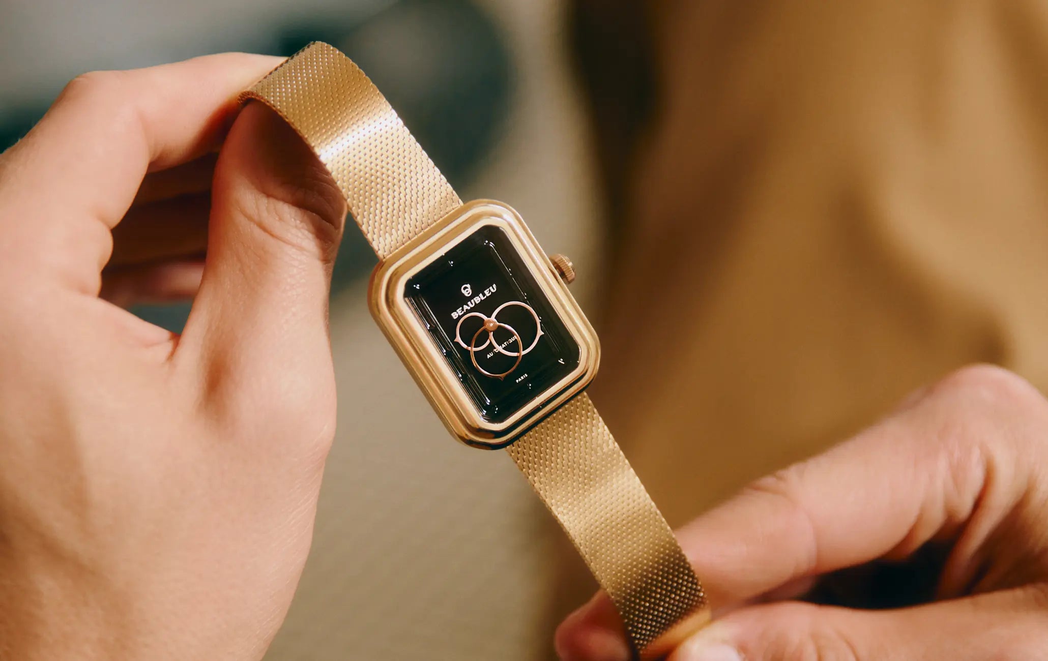 Montre automatique Ecce Figura Onyx tenue entre deux mains, cadran visible en gros plan avec son bracelet en maille or rose