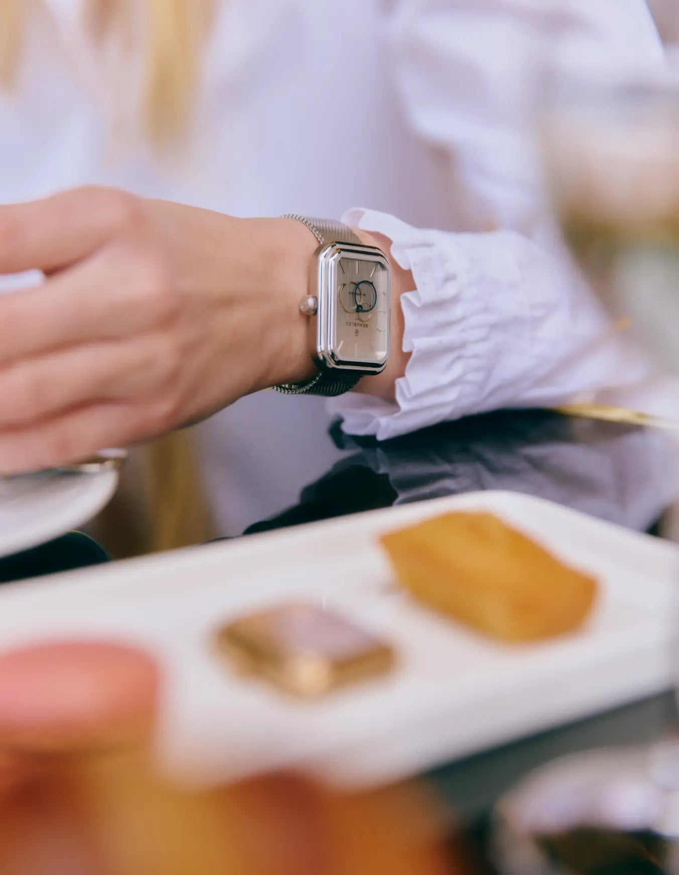 Montre automatique Ecce Figura Vesperal en arrière plan portée par une femme à la terrasse d'un café