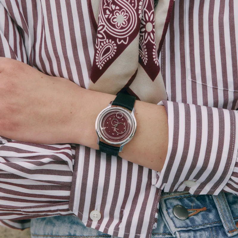 Montre Beaubleu La Pièce Lie de Vin avec bracelet grainé portée au poignet d'une femme avec une chemise à rayures