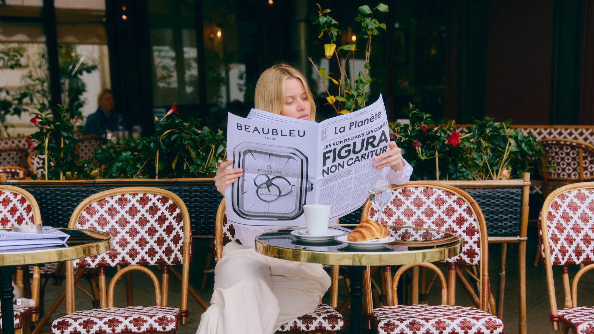 Femme à la terrasse d'un café tenant un journal parlant de la nouvelle collection Beaubleu Ecce Figura