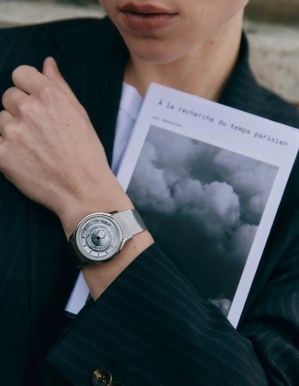 Montre Beaubleu La Pièce Acier portée au poignet d'une femme en costume avec un livre à la main