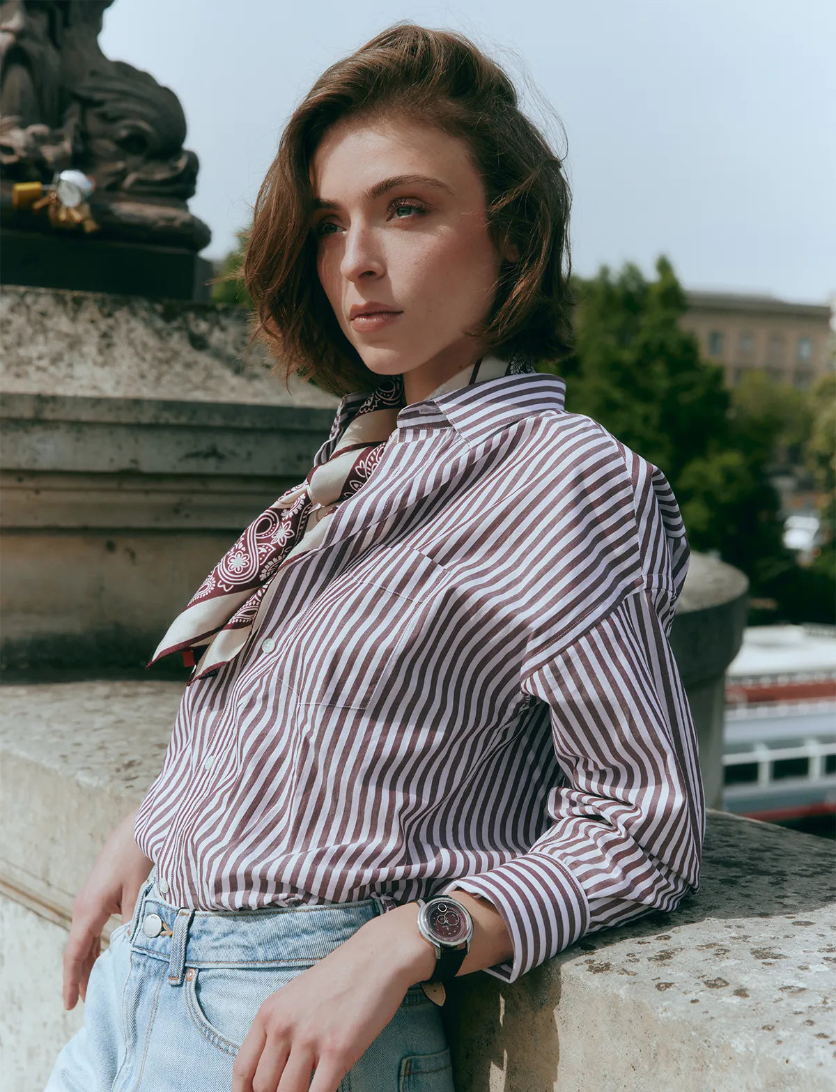 Montre La Pièce Lie de Vin portée au poignet d'une femme avec une chemise à rayures