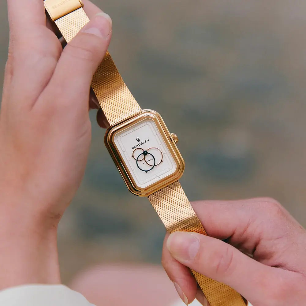 Gros plan de mains tenant une montre avec un bracelet en maille tressée or rose