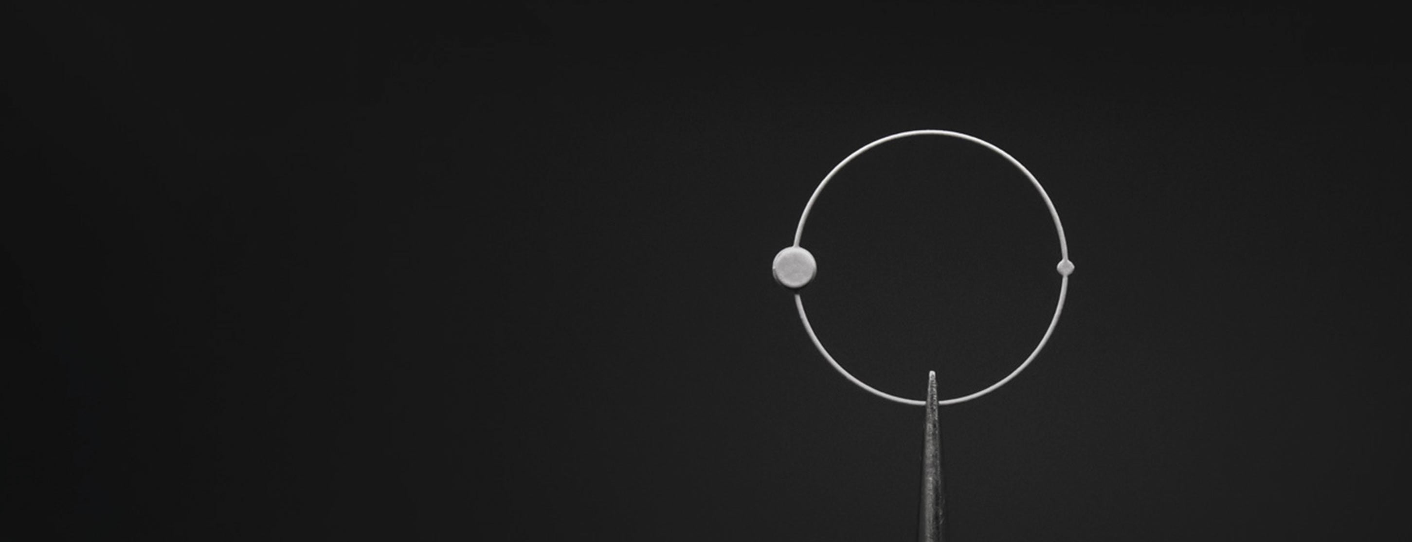 Photo en gros plan d'une aiguille ronde Beaubleu maintenue par une pince d'horloger sur un fond noir