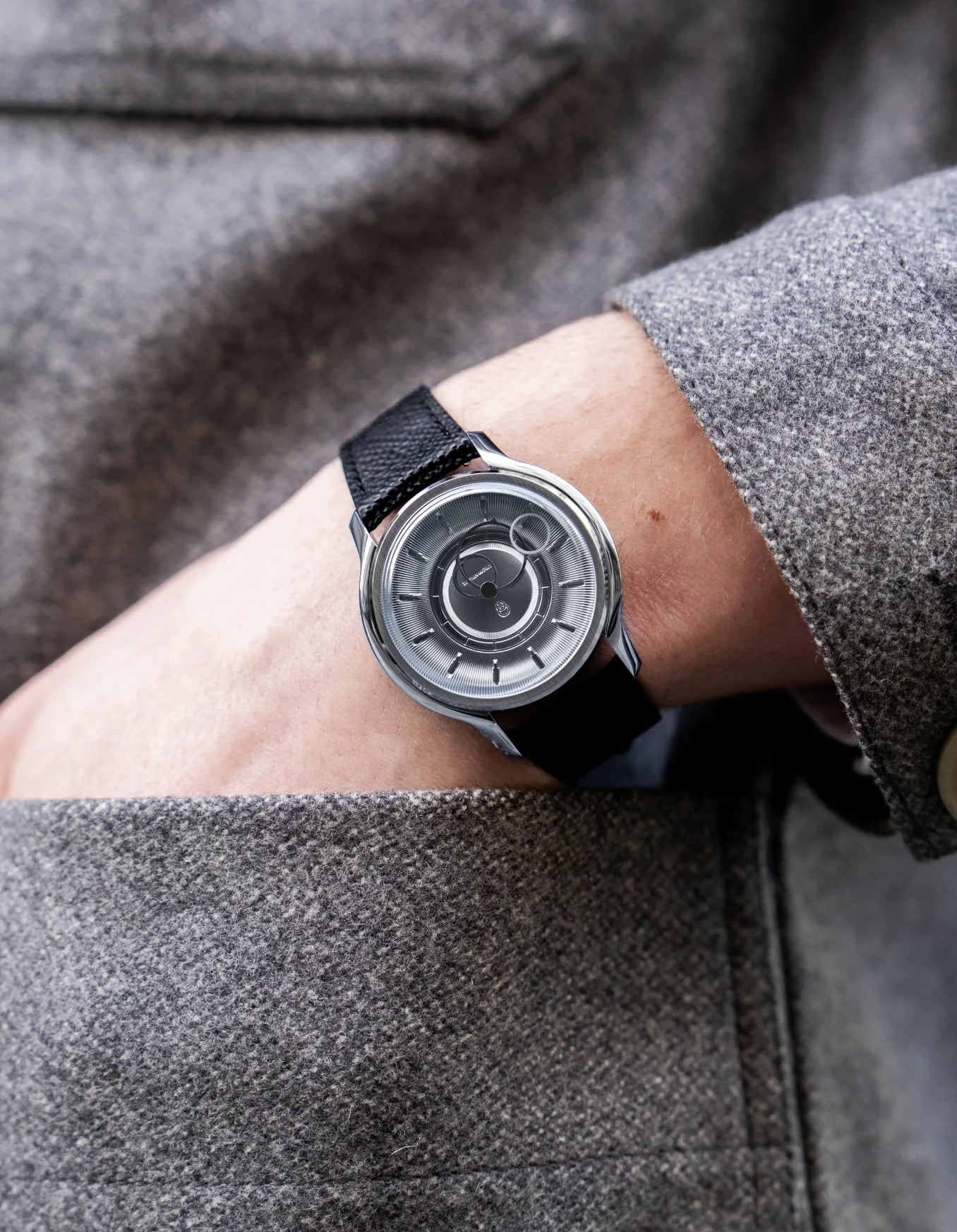 Montre Beaubleu La Pièce cadran acier avec bracelet cuir grainé noir portée au poignet avec une veste grise