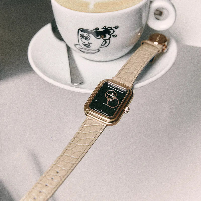 Montre Beaubleu Figura Onyx posée près d’un café, équipée du bracelet Flat White en cuir d’alligator