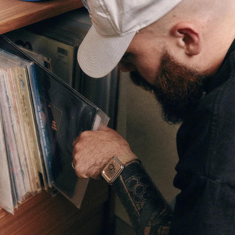 Homme parcourant une collection de vinyles avec une montre Beaubleu portée sur bracelet Flat White couleur crème