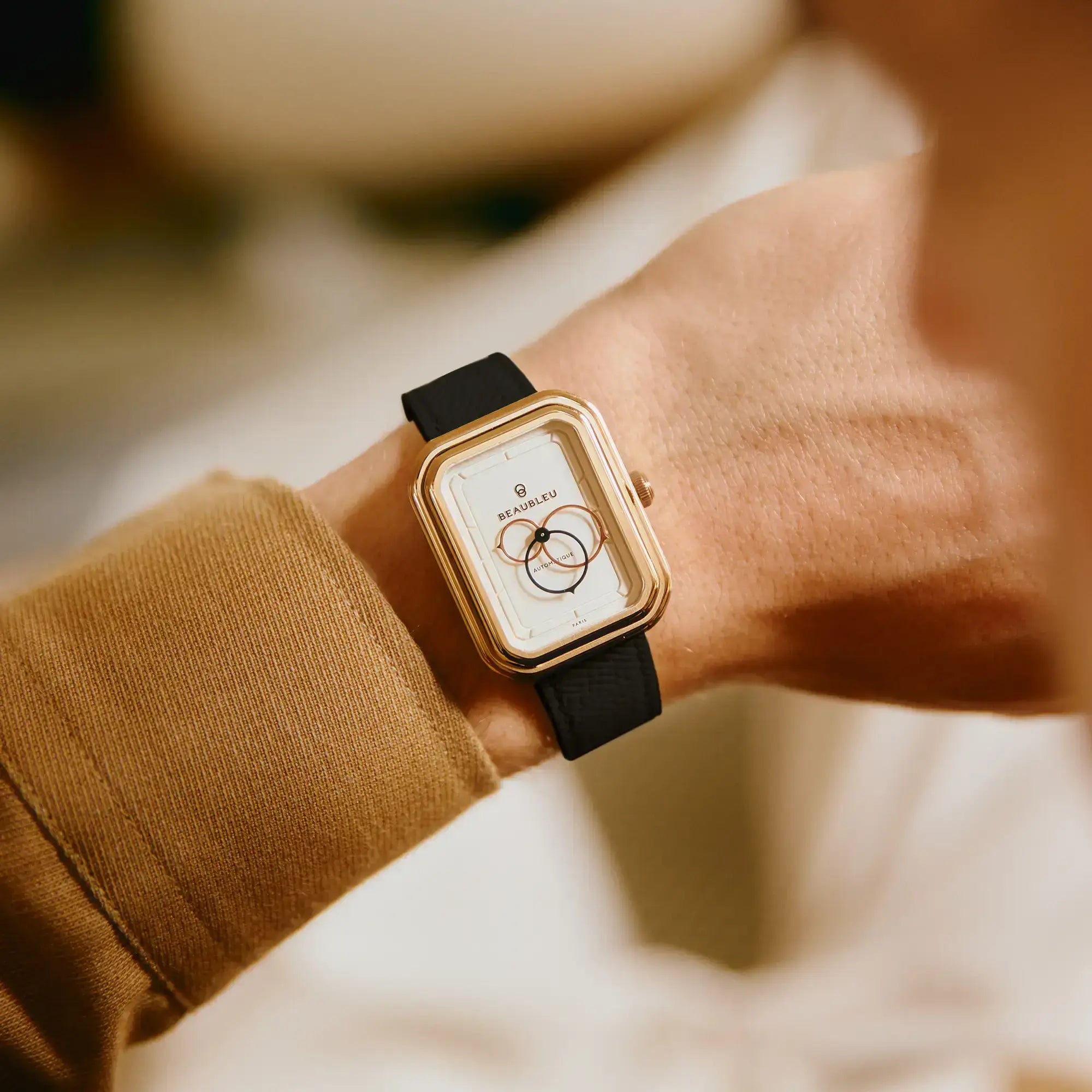 Montre automatique Ecce Figura Lys au boîtier doré portée sur un poignet masculin habillé d'une veste beige