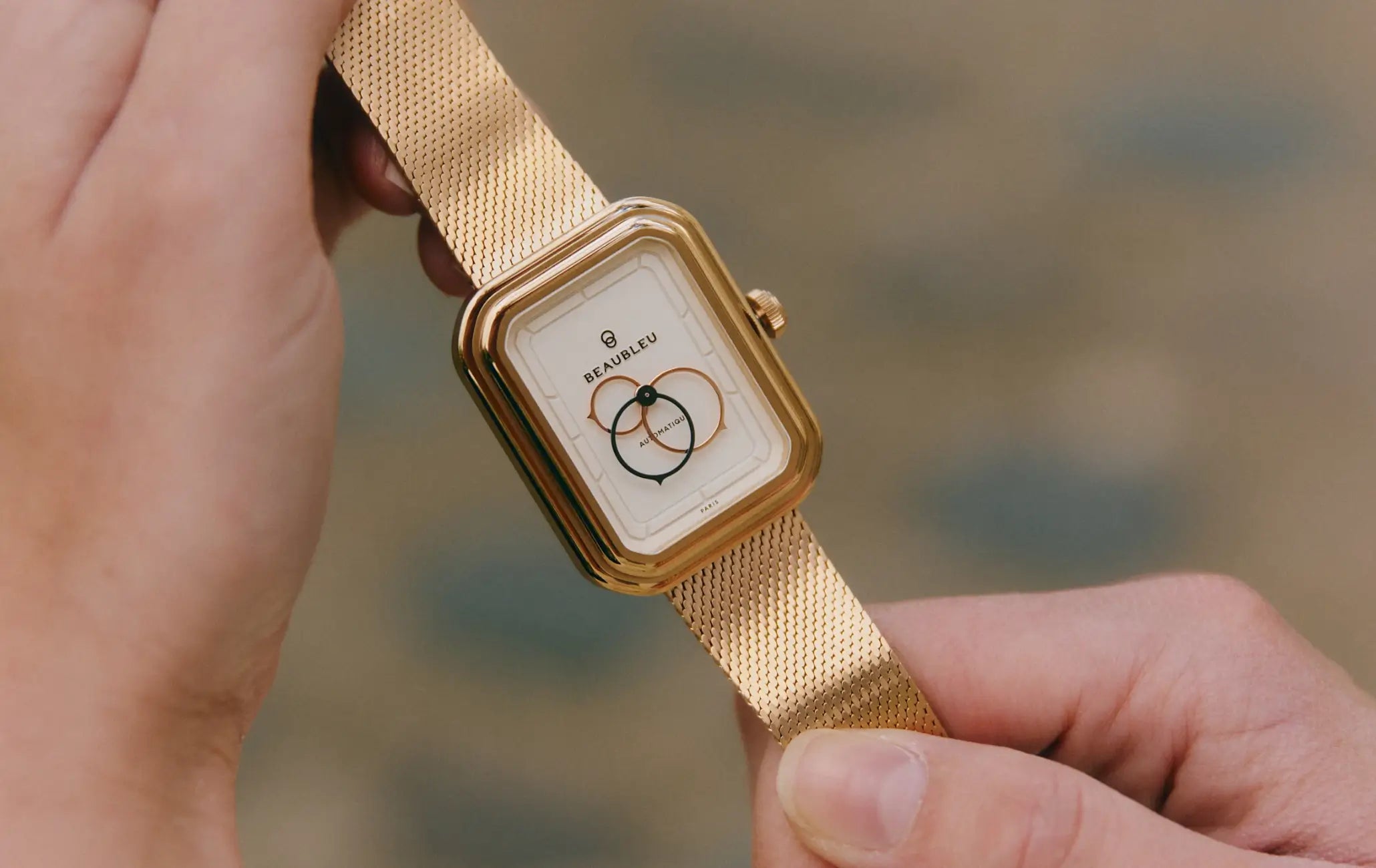 Montre automatique Ecce Figura Lys tenue entre deux mains, cadran visible en gros plan avec son bracelet en maille or rose