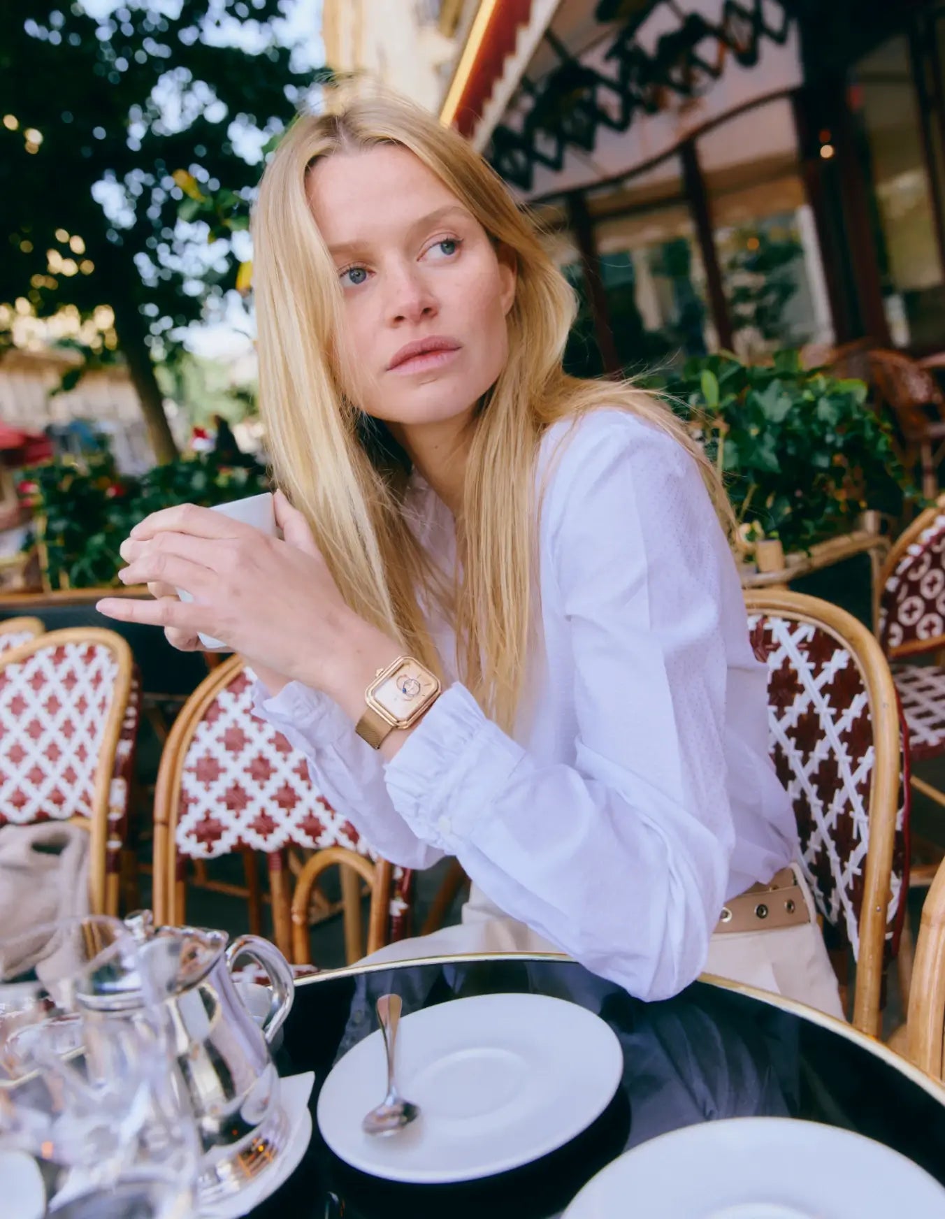 Femme assise à la terrasse d’un café, portant une montre Figura Sienna en or rose