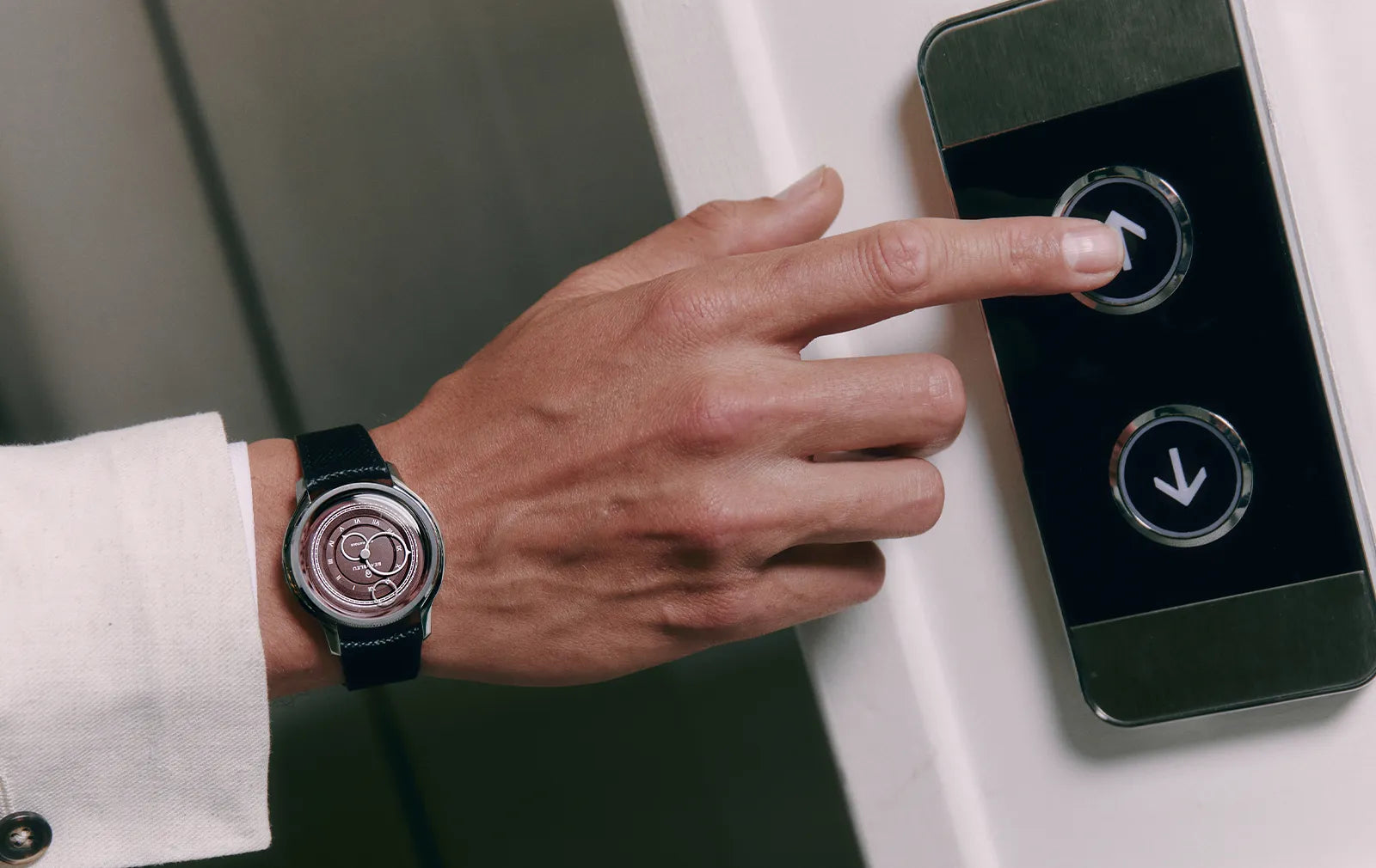 Montre La Pièce Lie de Vin de Beaubleu portée au poignet d'un homme en costume appuyant sur le bouton d'un ascenseur