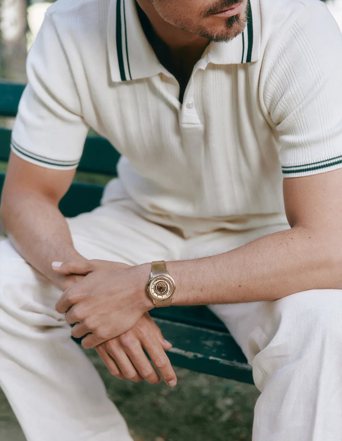 Homme assis sur un banc portant un polo blanc et une montre La Pièce en Or Rose avec un bracelet en maille
