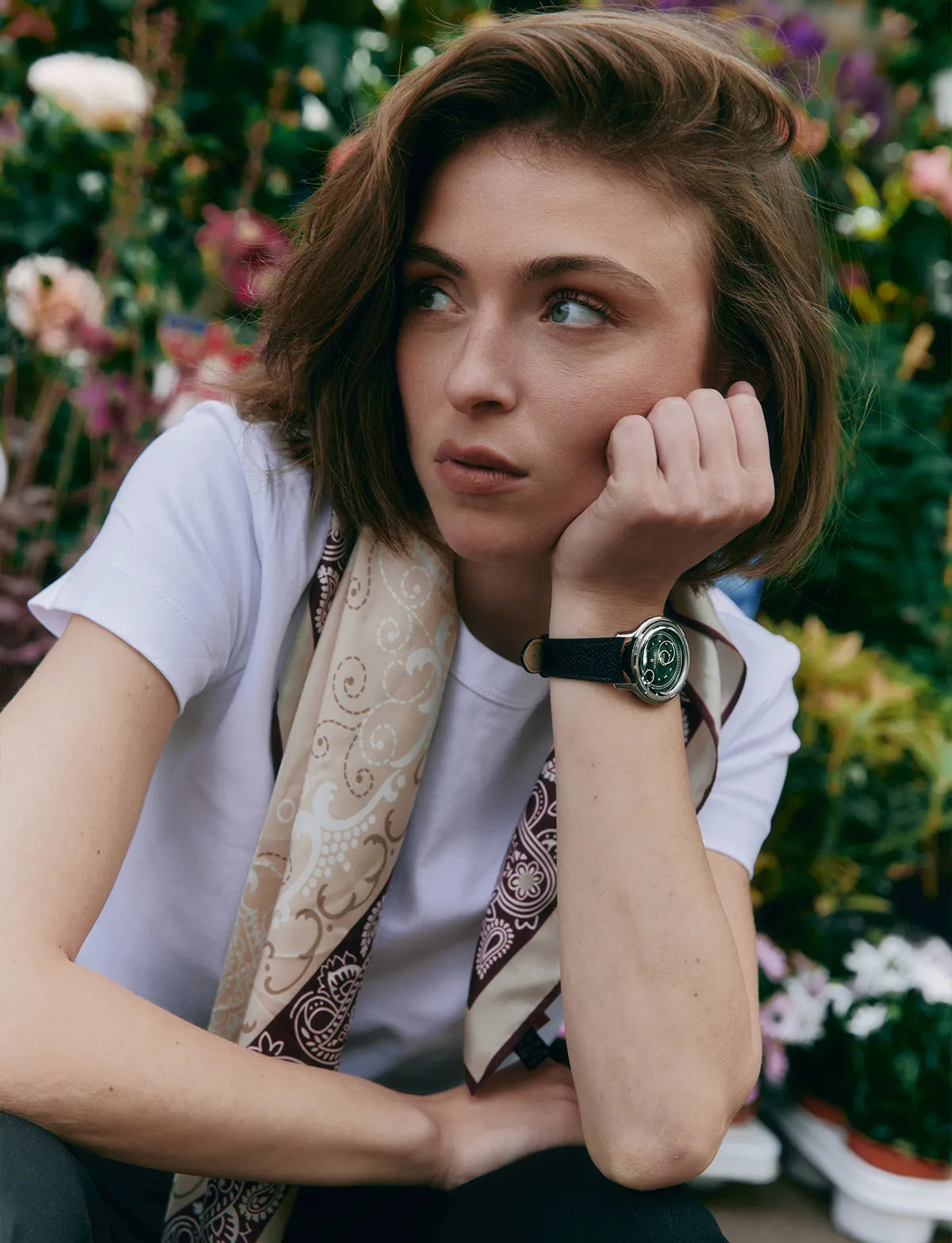 Femme portant la montre La Pièce Vert Olive de Beaubleu assise dans un jardin fleuri