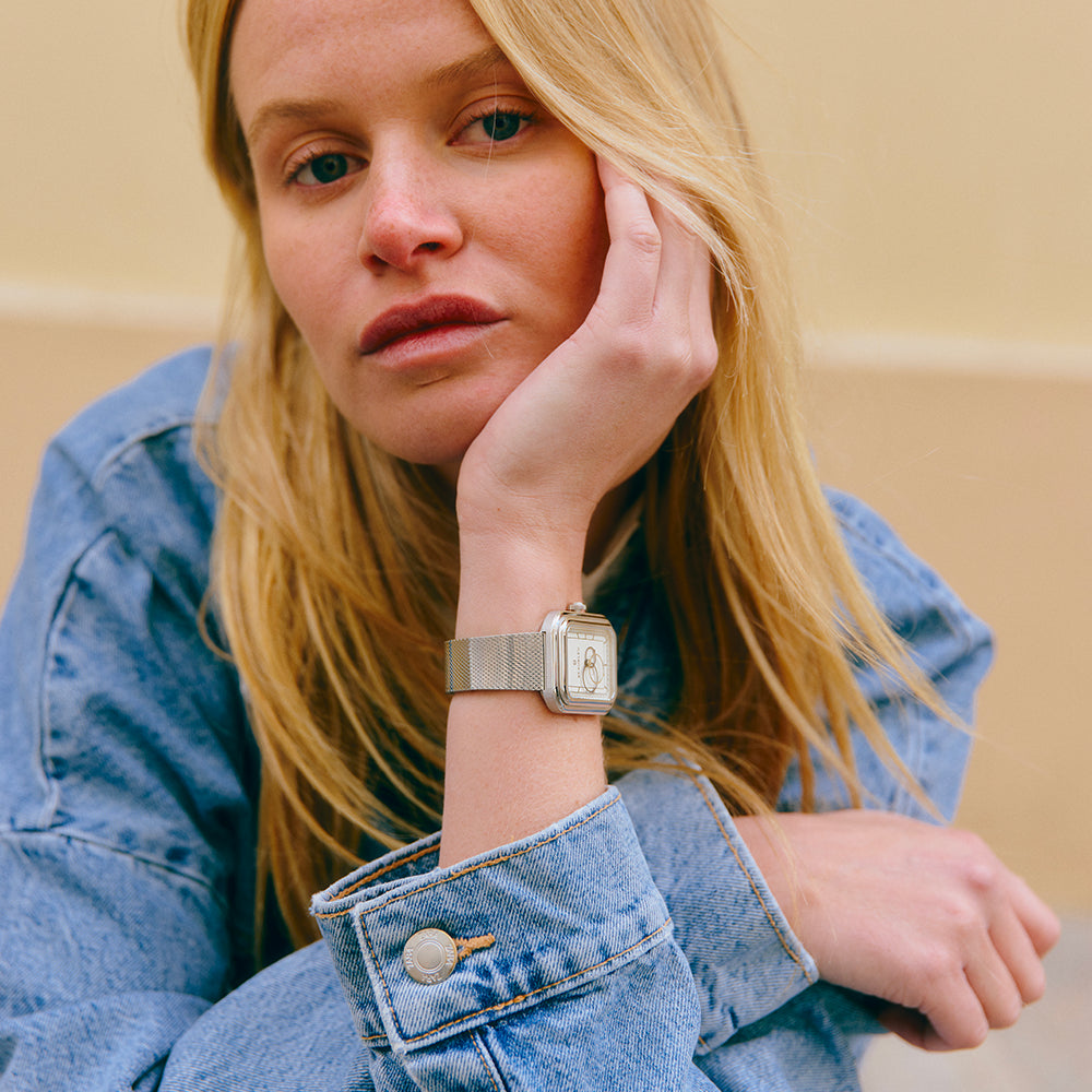 Une femme blonde en veste en jean pose en regardant l’objectif, portant une montre Beaubleu, modèle Figura Alba au bracelet en acier