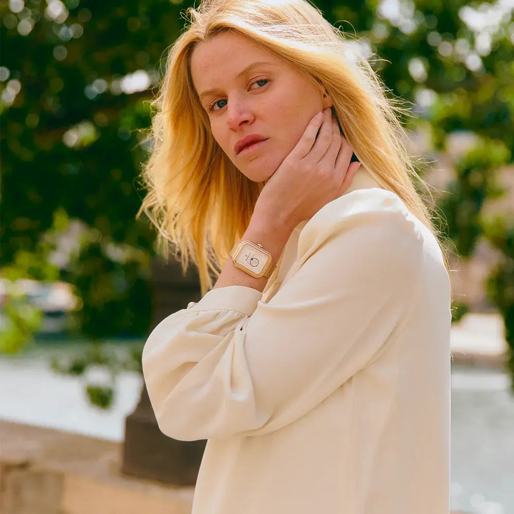 Une femme blonde pose en regardant l’objectif, portant une montre automatique Ecce Figura Lys au bracelet métallique en or rose