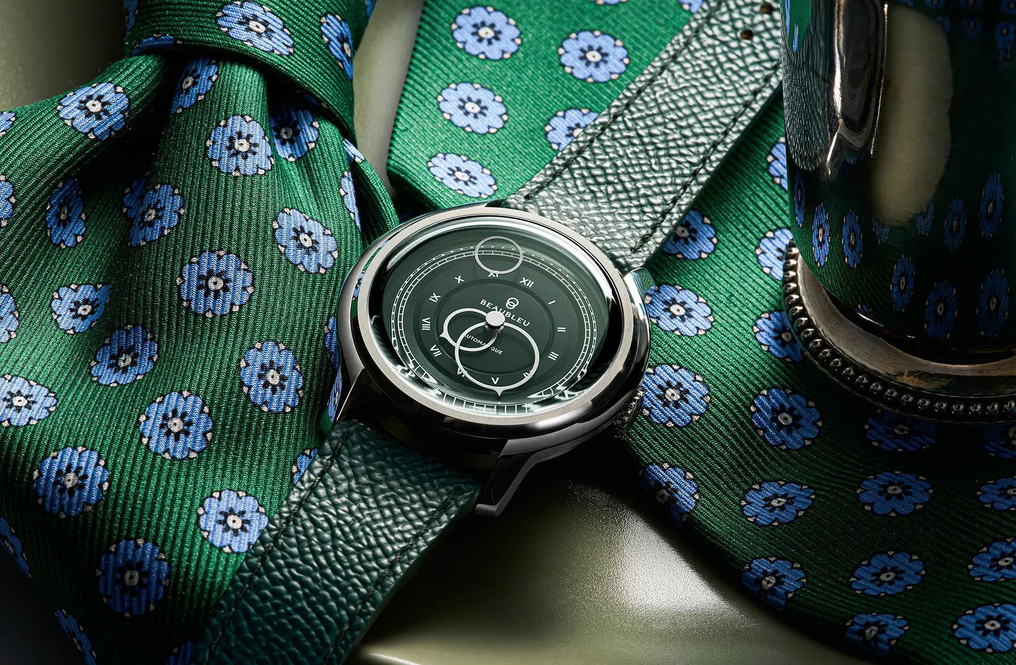 Montre La Pièce Olive de Beaubleu cadran vert posée sur une cravate verte avec des fleurs bleues