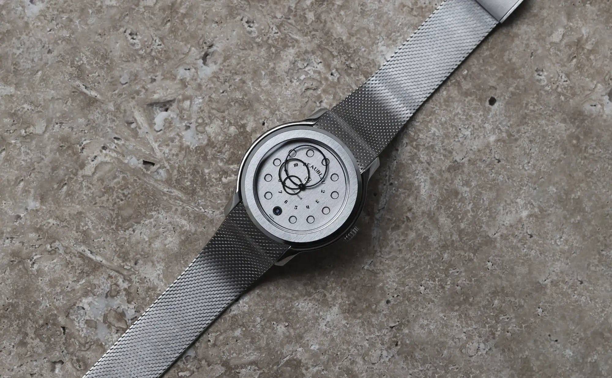 Montre Beaubleu Vitruve Date Acier avec bracelet acier tressé sur fond en pierre 