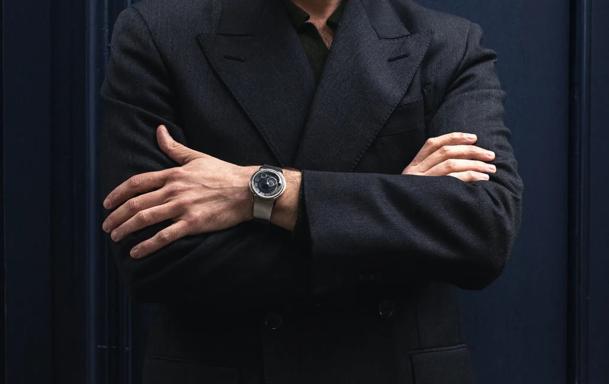 Montre Beaubleu La Pièce cadran noir avec bracelet acier portée au poignet d'une personne en costume avec les bras croisés